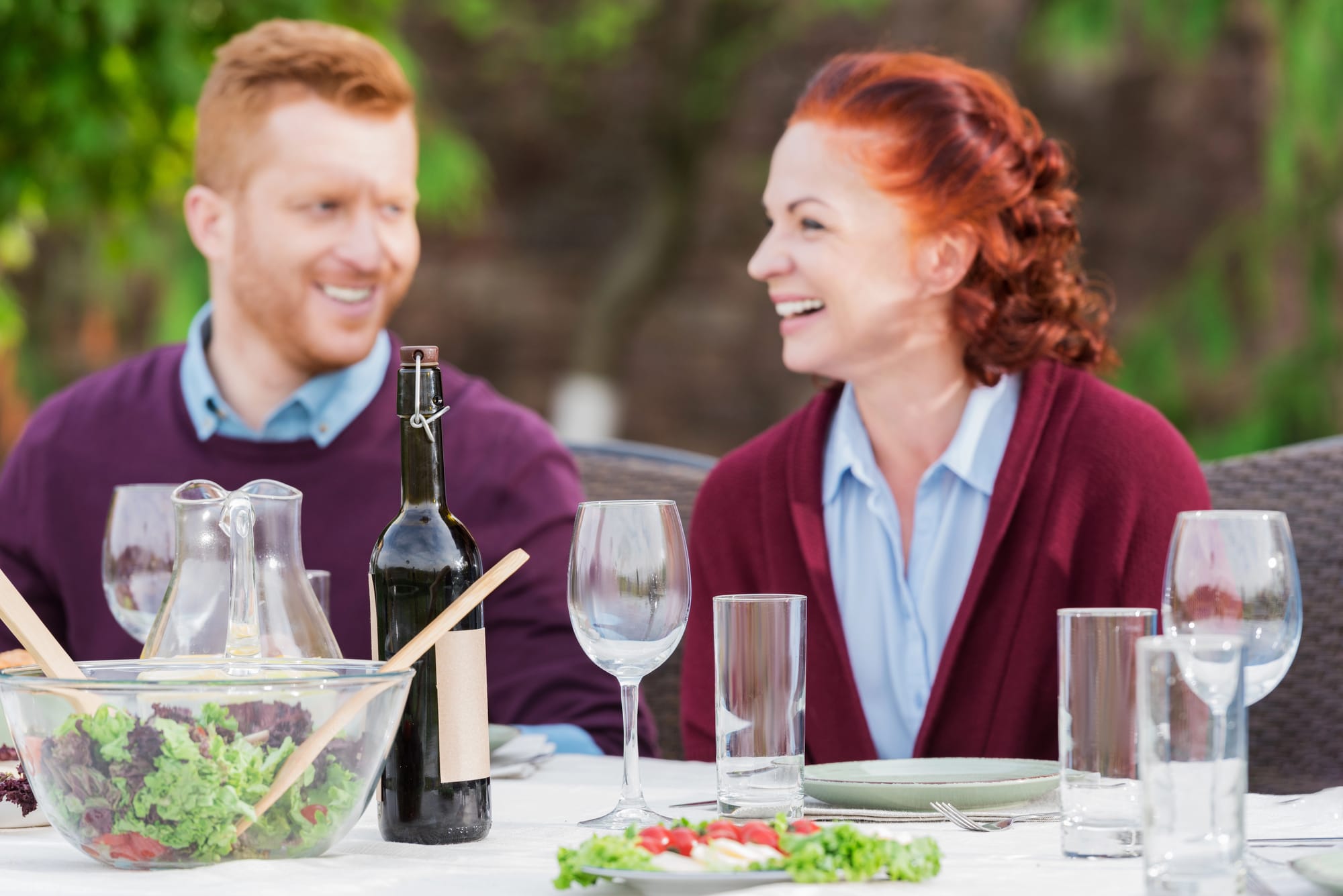 Smiling couple enjoys outdoor meal with wine.